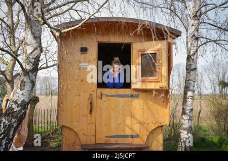 Kienitz, Germania. 12th Apr 2022. Il vacanziere berlinese Claudia Kleiner si appoggia sul 'Erlenhof' nella porta a metà aperta della carovana 'chäfchenglück' del pastore. La fattoria vacanze nel Medio Oderbruch offre vacanze natura-orientata da aprile a ottobre su un sito spazioso e pernottamento in sei caravan pastori, nonché in una cabina di legno. Un massimo di 15 ospiti possono trovare un posto dove dormire in azienda, e non ci sono né TV né radio nei vagoni e nella cabina. (A dpa: ' 'chäferstündchen im Schäferwagen' im Oderbruch') Credit: Soeren Stache/dpa/Alamy Live News Foto Stock