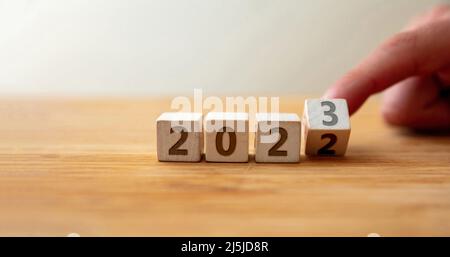 Dal 2022 al 2023 Felice Anno Nuovo. Il dito capovolge l'ultima cifra sul cubo di legno cambiando l'anno sul tavolo di legno. Nuovo piano, business, carriera, target, su Foto Stock