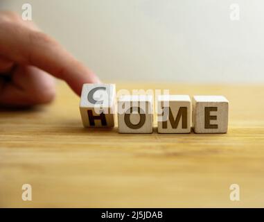 Come a casa concetto. La mano capovolge la lettera sul cubo di legno cambiando la sede della parola venire. Messaggio per il ritorno a casa, il benvenuto, insieme, ritorno a famiglia a h Foto Stock