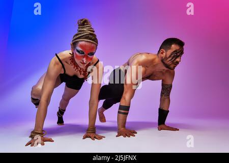 Bellissimi acrobati o ginnasti giovani con coloratissima pittura facciale su sfondo rosa blu sfumato. Balletto professionale coppia danza, emozionale duetto Foto Stock