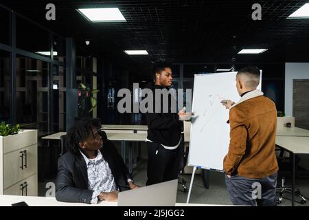 Discussione sul grafico delle criptovalute e dei bitcoin da parte di investitori multietnici. Gli uomini d'affari africani e asiatici stanno discutendo del luogo economico finanziario Foto Stock