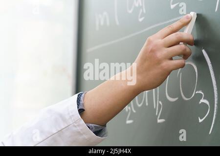 Primo piano della mano dello scienziato con un gesso che scrive un'equazione chimica Foto Stock