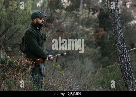 Giovane cacciatore che tiene il suo fucile in mezzo alla natura guardando verso il basso Foto Stock