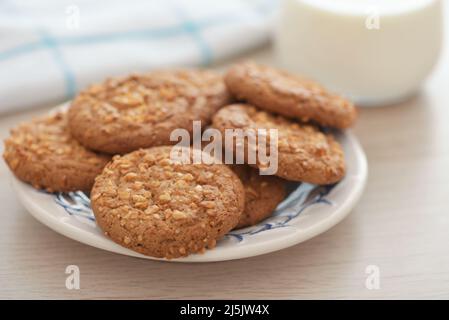 Primo piano di biscotti di farina d'avena con briciole di arachidi e un bicchiere di latte su un tavolo di legno Foto Stock