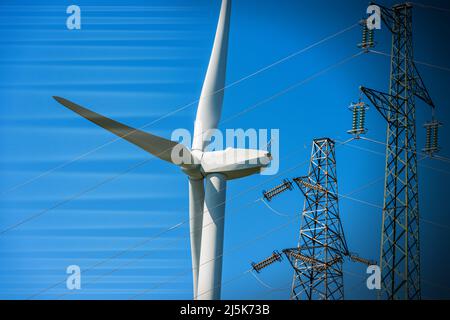 Primo piano di una turbina eolica bianca e di torri ad alta tensione (linea elettrica) contro un cielo blu chiaro. Concetto di energia rinnovabile. Foto Stock