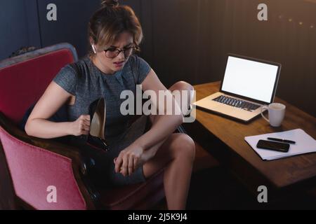 Donna d'affari con piedi doloranti dopo una lunga giornata lavorativa di indossare tacchi alti Foto Stock