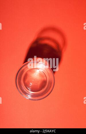 Bicchiere d'acqua con astratta ombra scura su sfondo rosso. Foto Stock