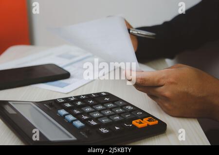 Uomo d'affari che usa la calcolatrice alla scrivania. Concetti di finanza aziendale, tasse e investimenti. Foto Stock