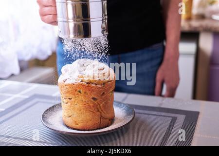 Aggiungere lo zucchero in polvere sulla gustosa torta di Pasqua su un piatto Foto Stock