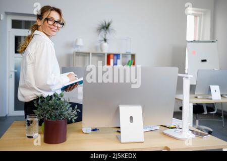 Ritratto di una donna allegra che si siede su una scrivania in ufficio Foto Stock