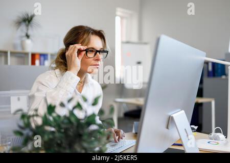 Donna di affari abbastanza matura in vetri funziona ad un calcolatore nell'ufficio. Segretario o contabile che lavora online Foto Stock