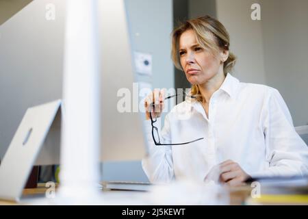 Una donna d'affari matura e pensiva con un'espressione preoccupata lavora a un computer in ufficio Foto Stock