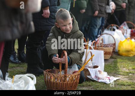 BUCHA, UCRAINA - APRILE 24, 2022 - Un ragazzo protegge una candela che brucia coronando un paska dal vento con le mani si siede prima di una cerimonia di consacrazione fuori della Chiesa di Sant'Andrea il primo apostolo chiamato durante la celebrazione della Pasqua ortodossa a Buca che si sta riprendendo dai crimini di guerra commessi dalle truppe russe dopo La sua liberazione dagli invasori russi, la regione di Kiev, l'Ucraina settentrionale. Credit: Ukrinform/Alamy Live News Foto Stock