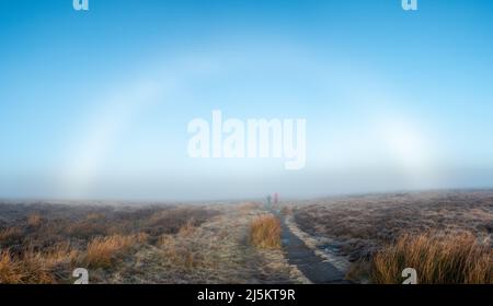 Camminatori in collina che camminano attraverso un fogbow su Ilkley Moor, West Yorkshire, UK tempo Foto Stock