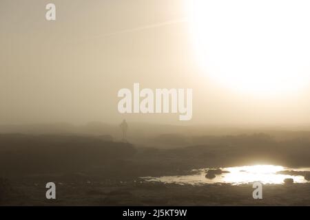 Caduto corridore che corre su brughiera nel sole mentre si rompe attraverso la nebbia e si riflette su una pozzanghera. Ilkley Moor, Regno Unito tempo - nebbia giorno Foto Stock