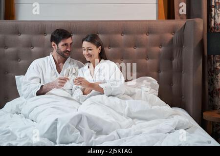 Coppia che si accoppiano i loro bicchieri nel letto dell'hotel Foto Stock