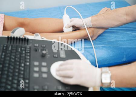 Specialista medico che esegue ultrasuoni doppler dei vasi degli arti inferiori Foto Stock