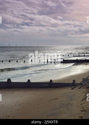 Onde che si infrangono su Frinton Beach, con la luce del sole che si infrangono attraverso nuvole di tempesta che si riflettono in una luce soffusa e brillante dalla sabbia scintillante. Foto Stock