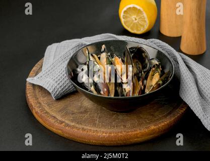 cozze in salsa cremosa in un piatto nero su sfondo nero Foto Stock