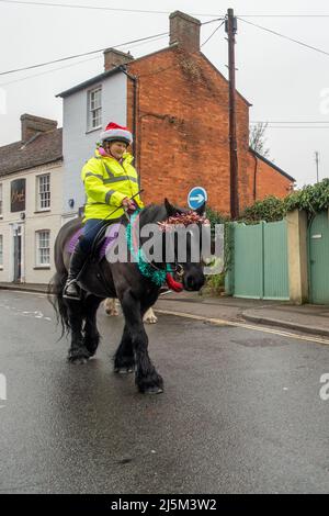 Femmina che indossa un cappello di Natale a cavallo nero vestito in tinsel lungo una strada nel centro di Newport Pagnell, Buckinghamshire, Engla Foto Stock