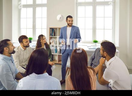 Gruppo di persone diverse che siedono in cerchio e ascoltano con attenzione il loro collega maschile in riunione. Foto Stock