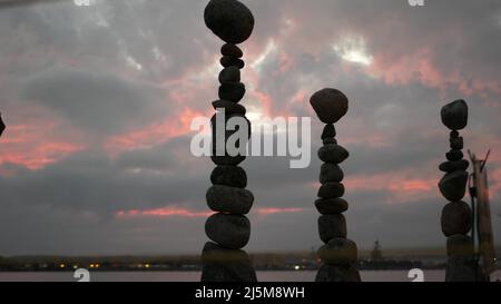 Bilanciamento della roccia contro cielo nuvoloso e drammatico al tramonto. Pila di pietre in equilibrio, piramide stabile nel crepuscolo rosa della sera. Nuvolosità al tramonto dall'acqua marina dell'oceano. Concetto di buddismo. Foto Stock