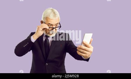 Il vecchio uomo in tuta legge le notizie sullo smartphone Foto Stock