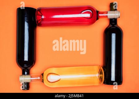 Diverse bottiglie di vino, rosso, bianco e rosato, incrociate tra loro, su sfondo arancione. Foto Stock