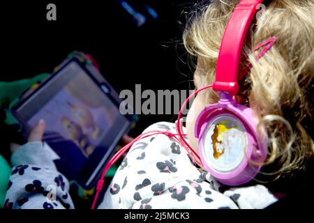 Ragazza di 3 anni che guarda cartoni animati sul suo iPad indossando le cuffie mentre viaggia. Foto Stock
