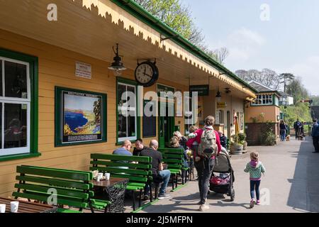 Passeggeri seduti al sole e in attesa del treno a vapore successivo alla stazione ferroviaria di Alresford sulla linea di Watercress. Hampshire, Inghilterra Foto Stock