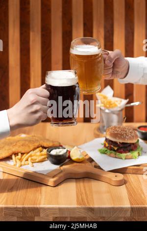 Primo piano di due mani che aggraffano birra bicchieri stein. Tostatura con una pinta di birre alla spina al banco del pub, toast con tazze di birra fredda al bar. Foto Stock