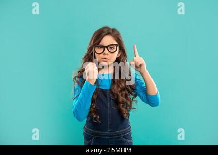 ragazza teen seria ispirata con idea ha capelli ricci tenere accessorio di partito di occhiali, partito Foto Stock