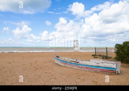 La vecchia barca di legno si trova capovolta sulla costa del Mar Nero, foto di paesaggio, la torre di salvataggio bianca è sotto il cielo nuvoloso su uno sfondo. Crimea Foto Stock