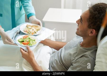 L'uomo felice che ottiene il pasto sul vassoio dal lavoratore del centro medico Foto Stock