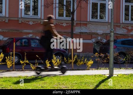 Movimento Blur giovane uomo che guida e-scooter sulla pista ciclabile in città, Sopron, Ungheria Foto Stock