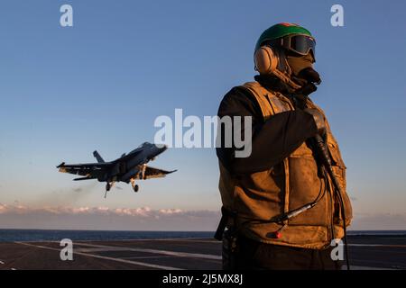 USS Ford, Stati Uniti. 19 aprile 2022. Un marinaio della Marina degli Stati Uniti si alza in piedi come un F/A-18E Super Hornet aereo da caccia assegnato al Golden Warriors of Strike Fighter Squadron 87 si prepara a atterrare sul ponte di volo della USS Gerald R. Ford, in corso durante le qualifiche del vettore, il 19 aprile 2022 nell'Oceano Atlantico. Credit: MC2/Minneee.de/Minne.de/Minne.de Live News Foto Stock