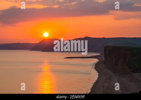 Burton Bradstock, Dorset, Regno Unito. 24th aprile 2022. Meteo Regno Unito. Il cielo si illumina di arancione al tramonto, visto da Burton Bradstock nel Dorset, mentre il sole scende dietro le scogliere di Golden Cap sulla Jurassic Coast alla fine di una calda giornata di sole. Picture Credit: Graham Hunt/Alamy Live News Foto Stock