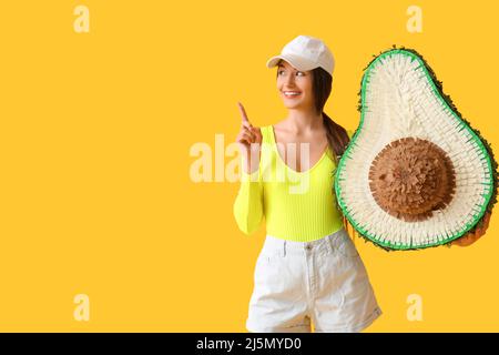 Giovane donna con pinata messicana che mostra qualcosa su sfondo giallo Foto Stock