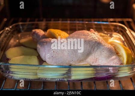Vassoio appena sfornato con coscia di pollo al limone, patate e cipolla rossa. Foto Stock