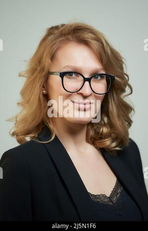 Una giovane donna elegante in occhiali con un vestito nero con una camicia nera. Foto Stock