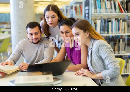 Simpatico gruppo di studenti in preparazione insieme per l'esame in una moderna biblioteca universitaria Foto Stock