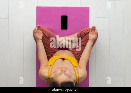 Donna incinta meditating a casa attendendo bambino che fa il codice prenatale in linea yoga la classe che si sieta in posizione del loto, esercitandosi nella meditazione per mentale sano Foto Stock