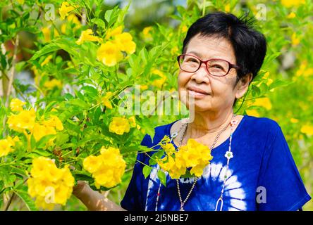 Ritratto di bella sorridente donna asiatica con fiore backgorund. Giornata internazionale delle persone anziane concetto. Foto Stock