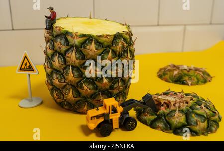 Mini costruzione in miniatura uomini che lavorano su un ananas. Affettare e tagliare. Foto Stock