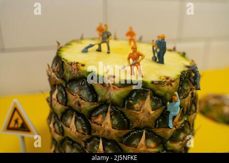 Mini costruzione in miniatura uomini che lavorano su un ananas. Affettare e tagliare. Foto Stock