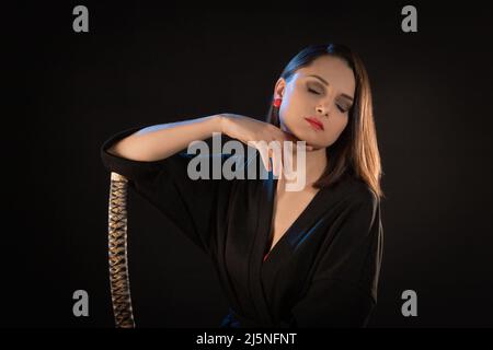 Ritratto di una giovane donna bruna pensiva con katana su sfondo nero. Foto Stock