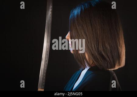 Ritratto di una giovane donna davanti ad una lama affilata su sfondo nero. Foto Stock