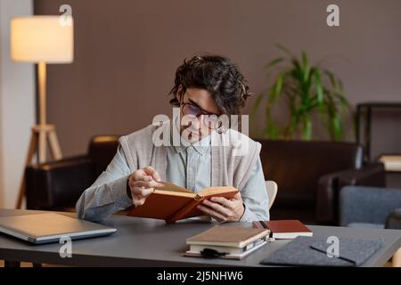 Scatto orizzontale medio dello psicologo professionale moderno seduto alla scrivania nel suo libro di lettura dell'ufficio mentre aspetta il cliente Foto Stock