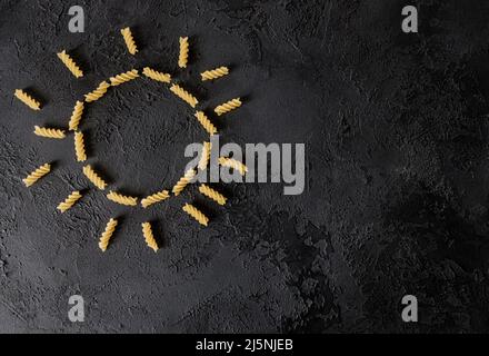 Pasta di fusilli cruda sotto forma di sole su una superficie scura. Cibo italiano Foto Stock