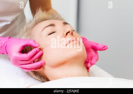 Ritratto di una donna bionda adulta su appuntamento di un cosmetologo. Procedura di ringiovanimento professionale. Un cosmetologo in guanti medici rosa applie Foto Stock